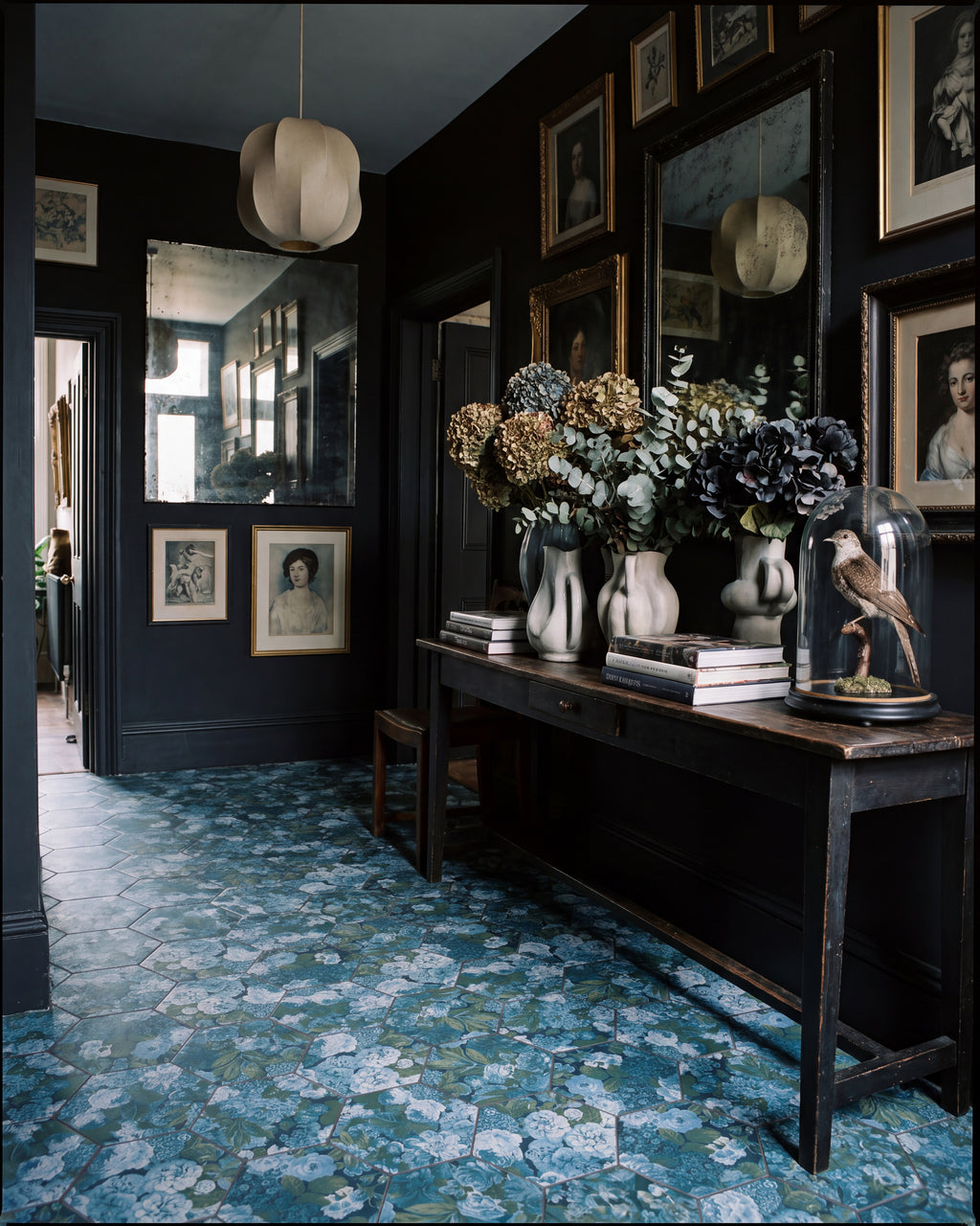 Sanderson Very Rose & Peony Pottery Blue Porcelain hexagons across the floor of a dark inky hallway, with a gallery wall of antique portraits, foxed mirrors and dried hydrangeas on a console table