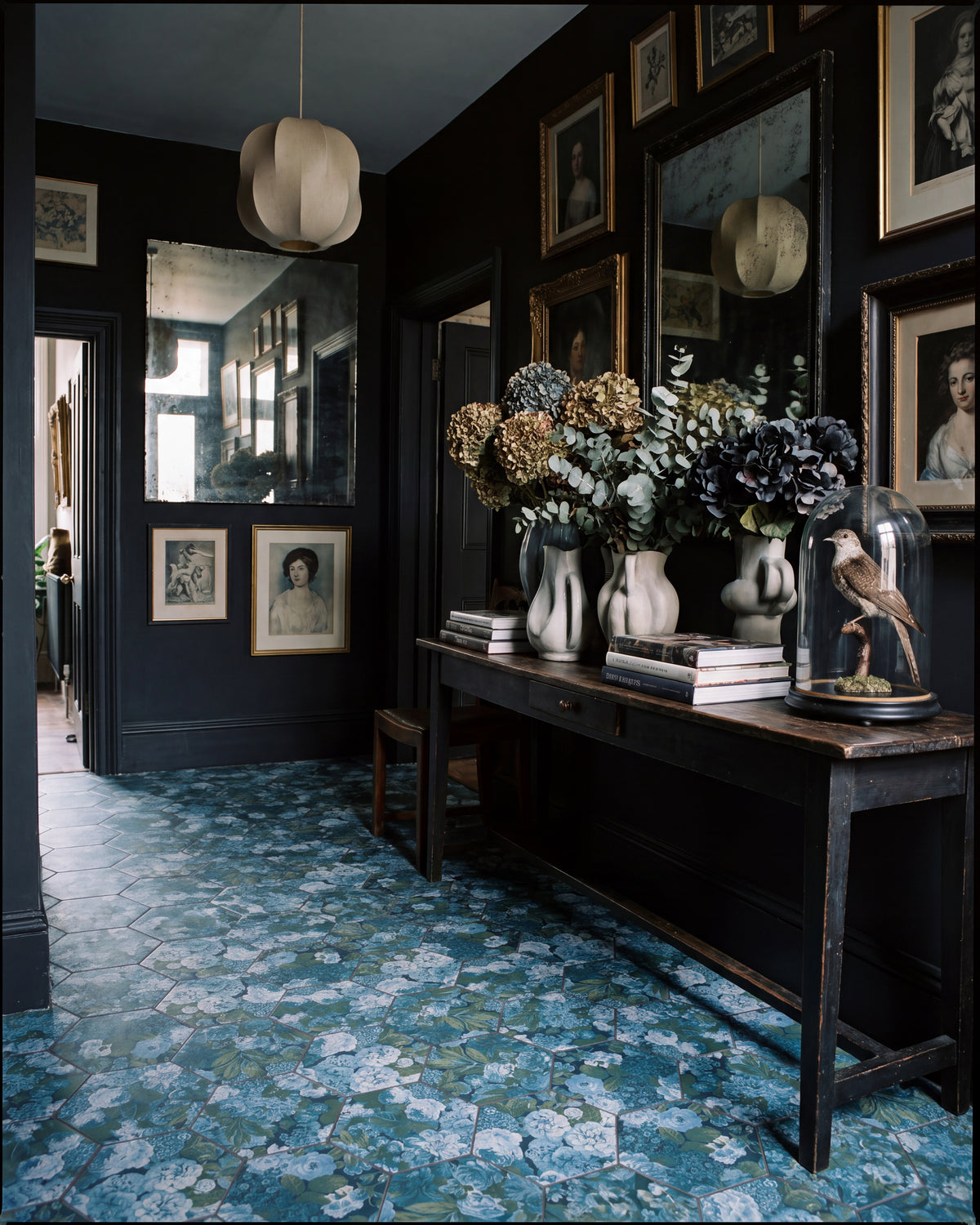 Sanderson Very Rose & Peony Pottery Blue Porcelain hexagons across the floor of a dark inky hallway, with a gallery wall of antique portraits, foxed mirrors and dried hydrangeas on a console table
