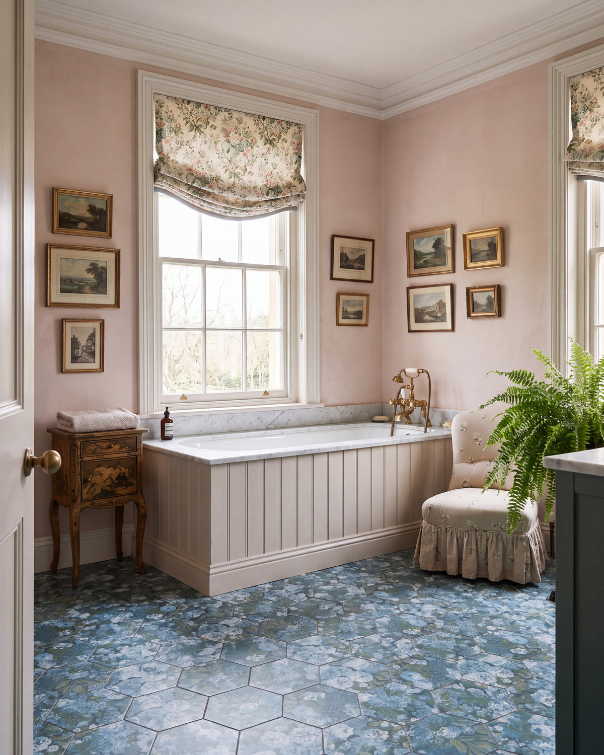 Sanderson Very Rose & Peony Pottery Blue Porcelain hexagons underfoot in a soft pink bathroom, with a marble-topped panelled bath, brass telephone taps and a wall of gilt-framed landscapes