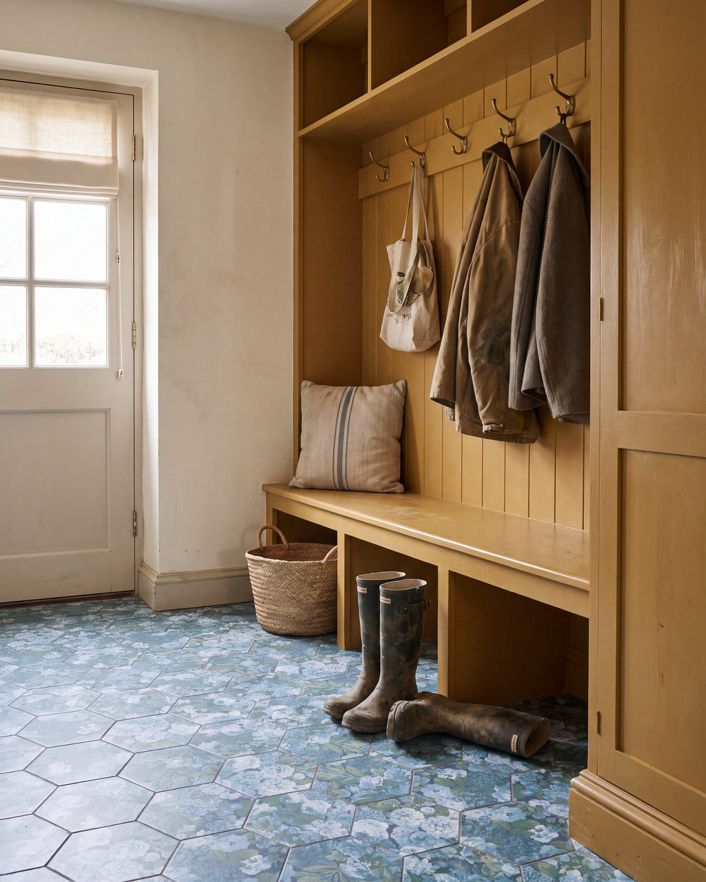 Sanderson Very Rose & Peony Pottery Blue Porcelain hexagons in a boot room with ochre-painted joinery, brass coat hooks, muddy wellingtons and a woven basket by a half-glazed back door