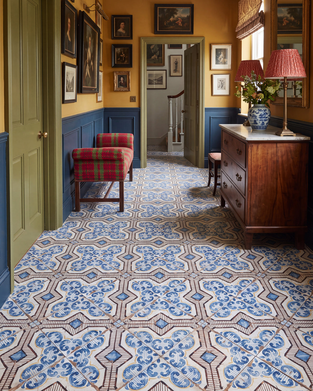 Sardinia Porcelain Gioia patterned tiles laid on the diagonal through a hallway with ochre walls, a deep blue panelled dado and a hang of antique portraits