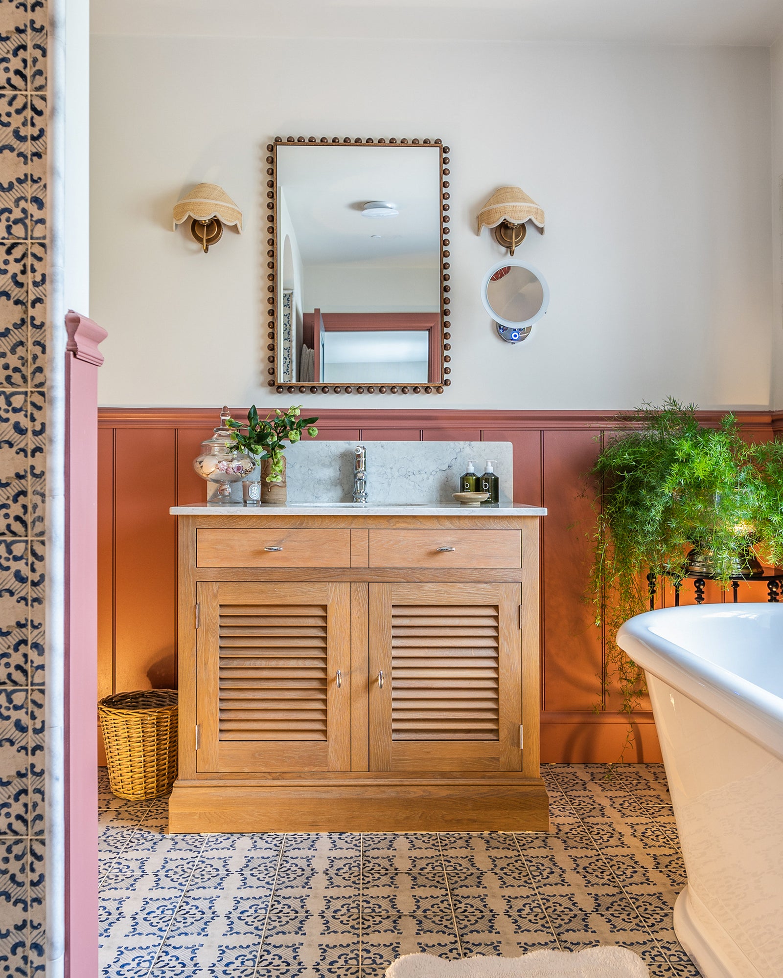 Sardinia Porcelain Tarricone across a bathroom floor beneath an oak louvred washstand with a marble top, against terracotta panelling and rattan wall lights. Interior design by Fiona Doswell Interiors