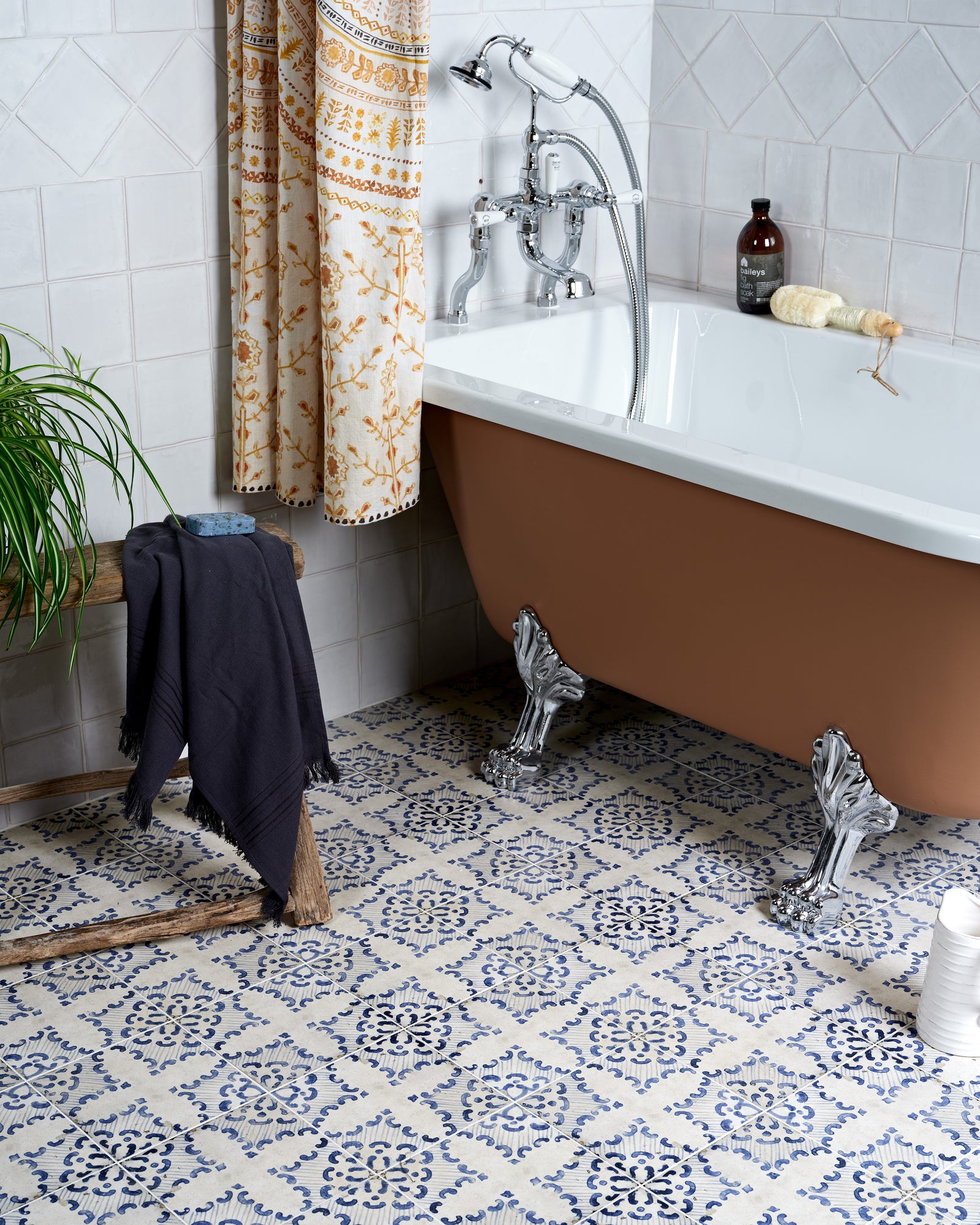 Sardinia Porcelain Tarricone underfoot around a terracotta-painted clawfoot bath, with St Ives Seashells tiles on the wall behind and a block-printed curtain. Brassware by Swadling
