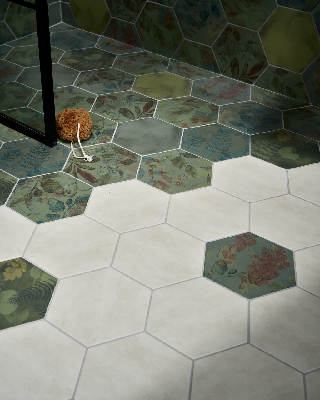 Shadow White Hex Field Porcelain laid across a bathroom floor, meeting a run of botanical patterned green hexagons at the wall