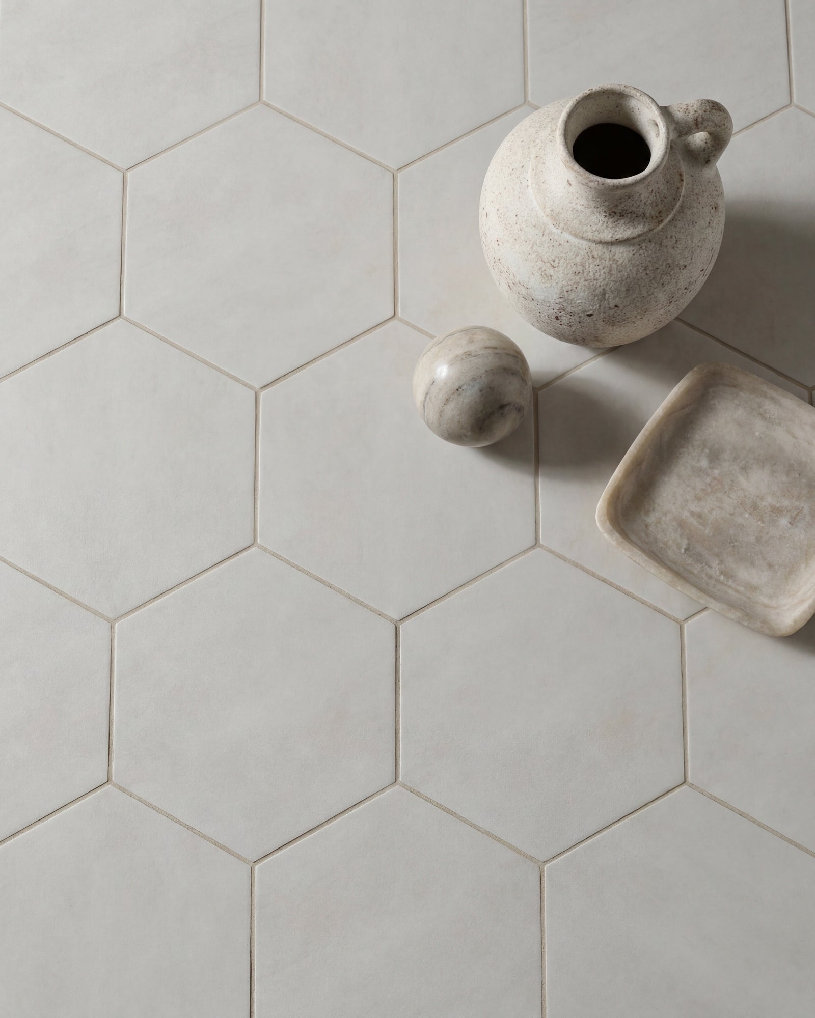 Shadow White Hex Field Porcelain in a close overhead view with a speckled stoneware jug, marble sphere and alabaster dish