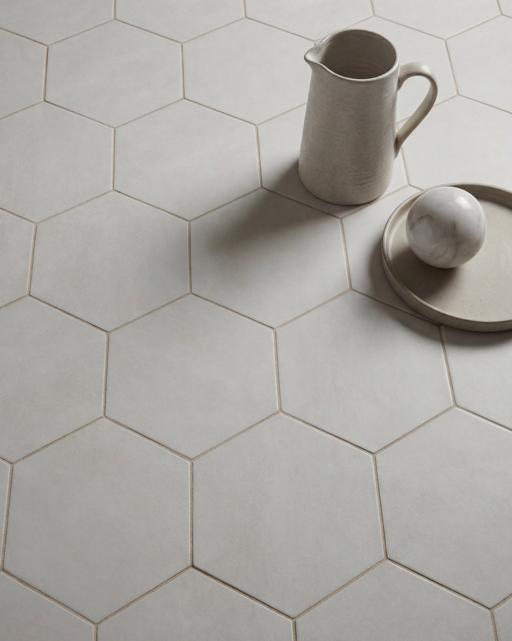 Shadow White Hex Field Porcelain in soft daylight with a cream ceramic jug and a marble sphere on a shallow dish