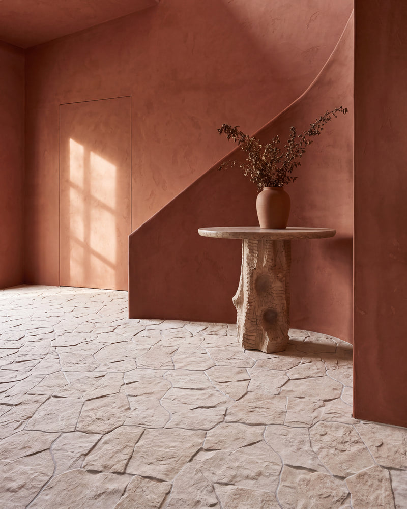 Sierra Porcelain Textured laid as a random crazy paving floor through a terracotta plaster hallway, running under the staircase past a stone side table and out towards a sunlit door