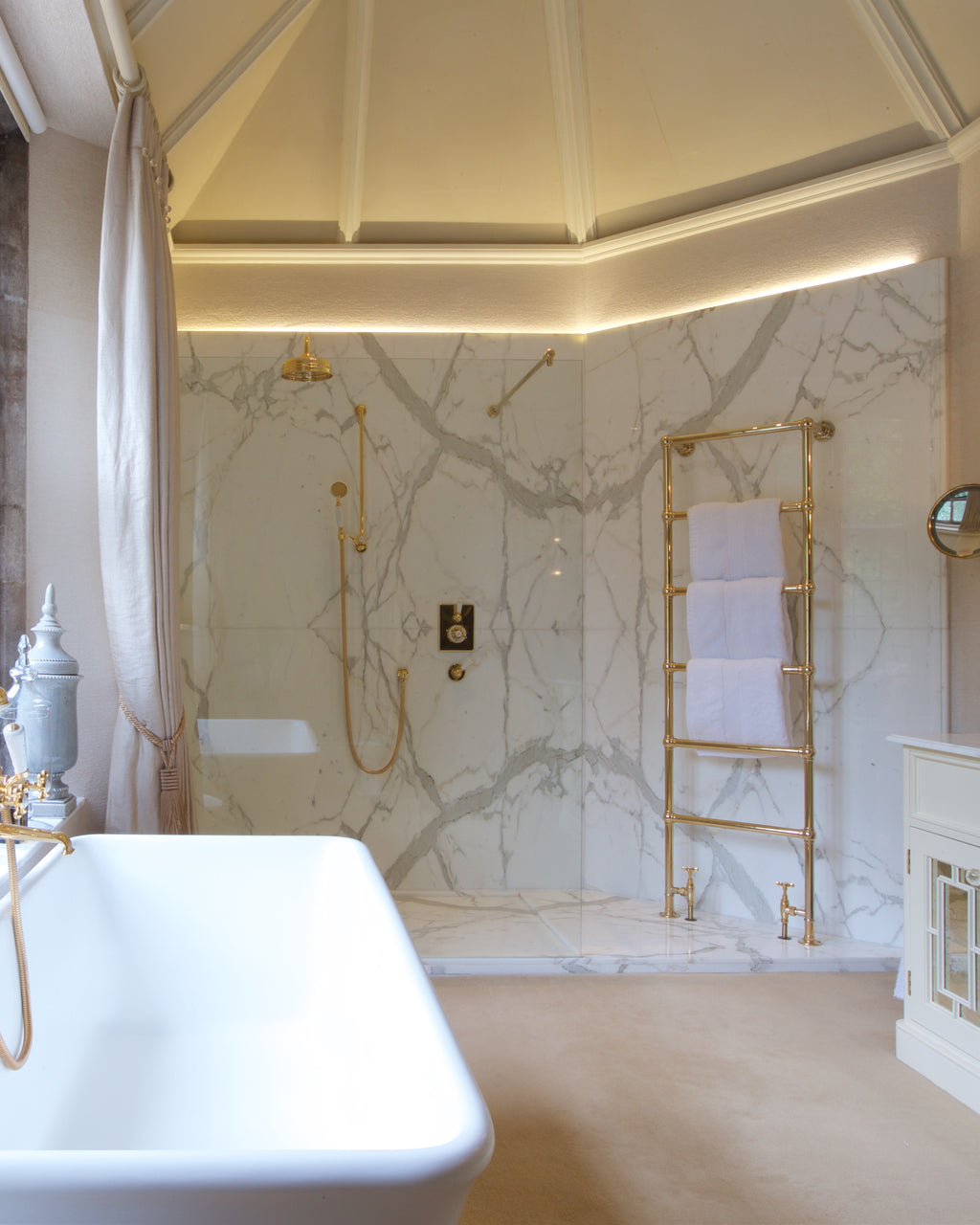 Statuario Marble Slab book-matched across a walk-in shower wall, seen past a freestanding bath, with a brass towel ladder and leaded windows