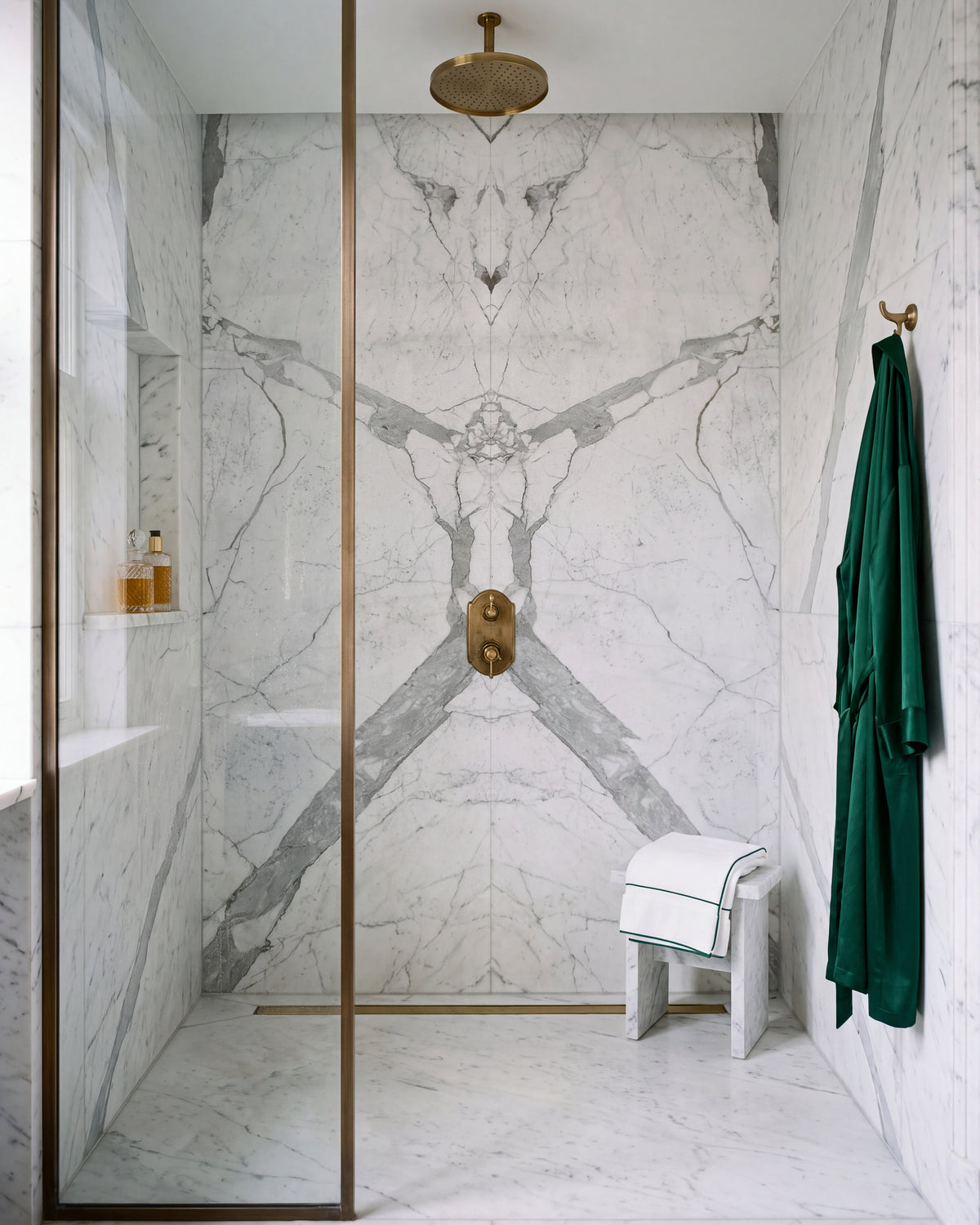 Statuario Marble Slab book-matched across the back wall of a walk-in shower, with a brass rain head, bronze-framed glass screen and a marble stool