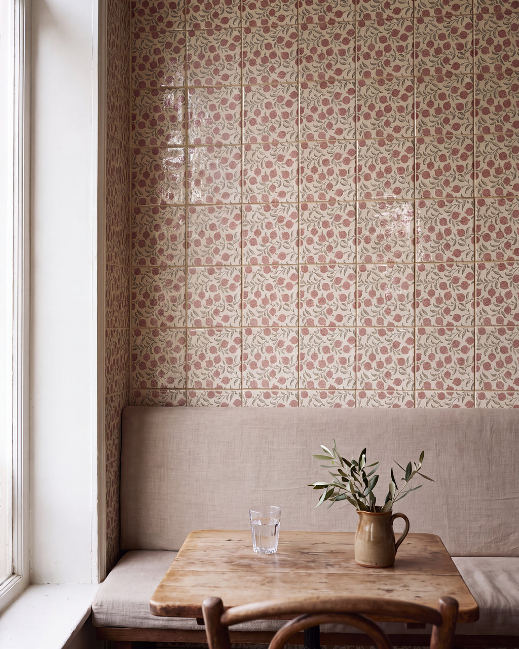 STUDIO Sanderson Anaar Pink Clay tiles running full height across a window-lit banquette corner, with a linen bench, worn wooden table and olive sprigs in a stoneware jug
