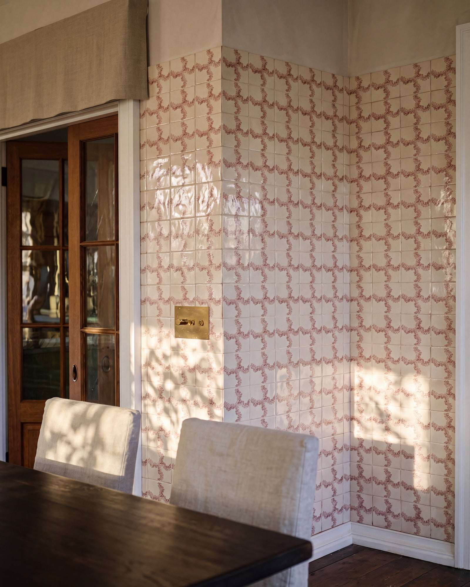 STUDIO Sanderson Oxbow Check Madder tiles wrapping a dining room corner in late afternoon light, with a dark timber table, linen slipcovered chairs, a glazed timber door and a brass switch plate