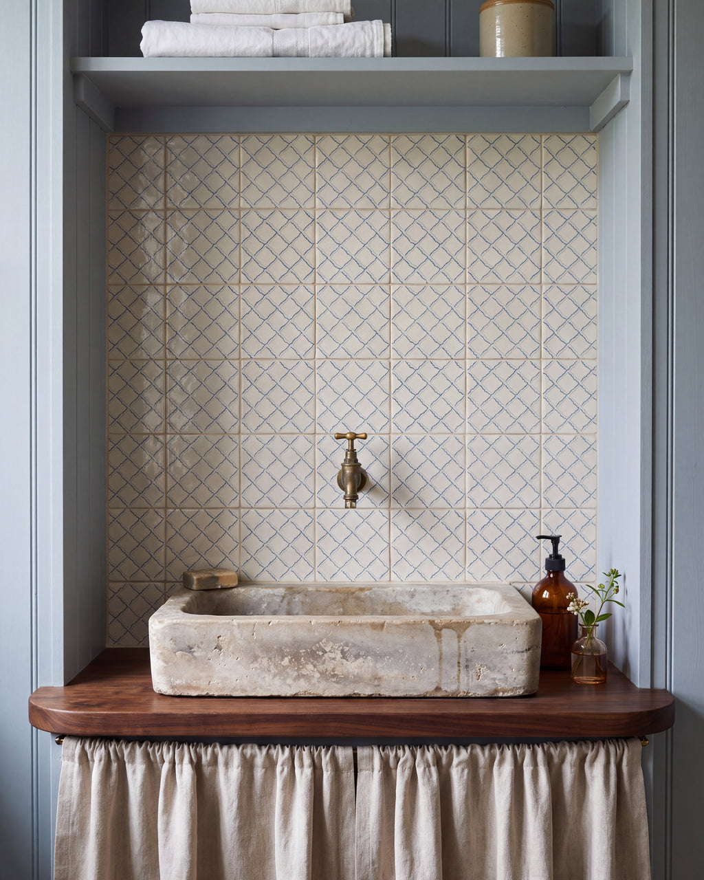 STUDIO Sanderson Rye Pottery Blue tiles forming a splashback behind an antique stone basin on a walnut washstand in a pale blue panelled cloakroom