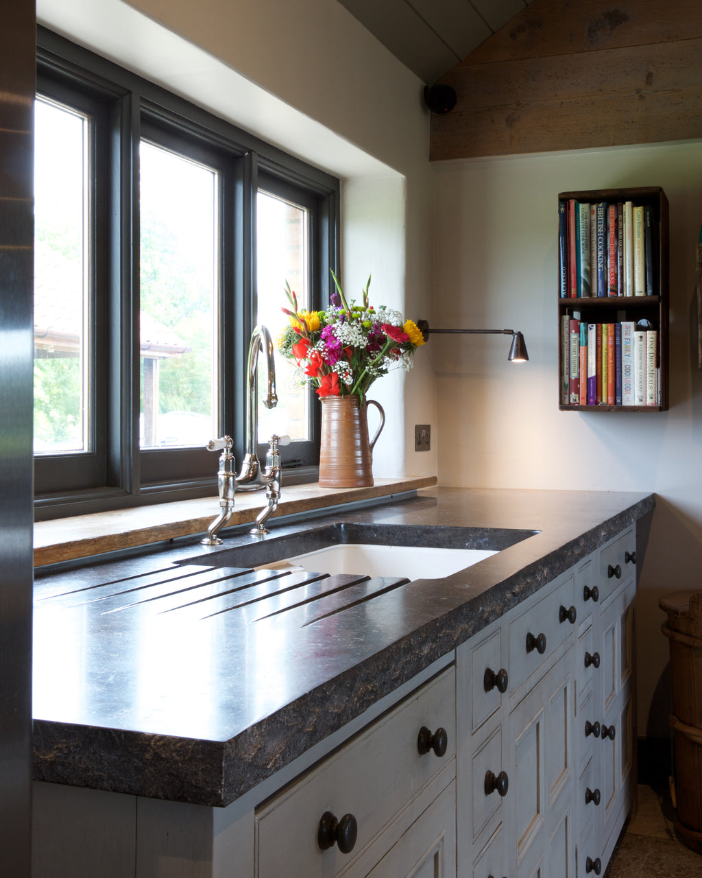 Tora Blue Honed Limestone Slab as a kitchen worktop with a grooved drainer and undermounted sink, beneath a run of windows in a vaulted room