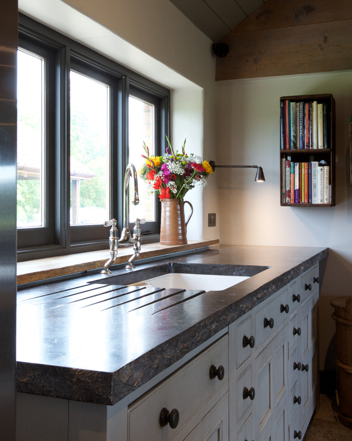 Tora Blue Honed Limestone Slab as a kitchen worktop with a grooved drainer and undermounted sink, beneath a run of windows in a vaulted room