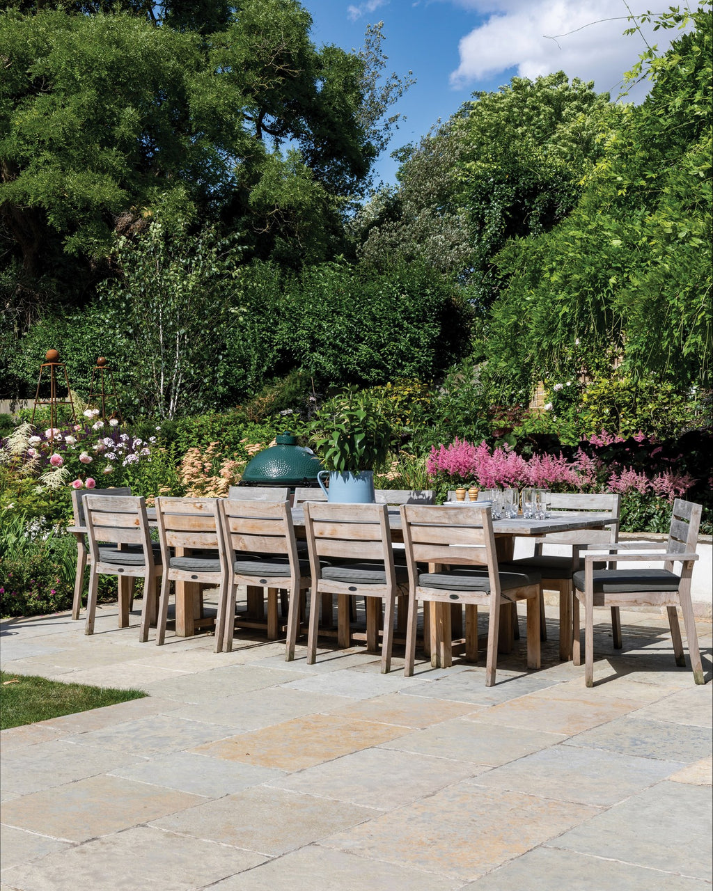 Trusloe Limestone Seasoned Finish paving on a walled garden terrace with a long teak dining table and deep flower borders