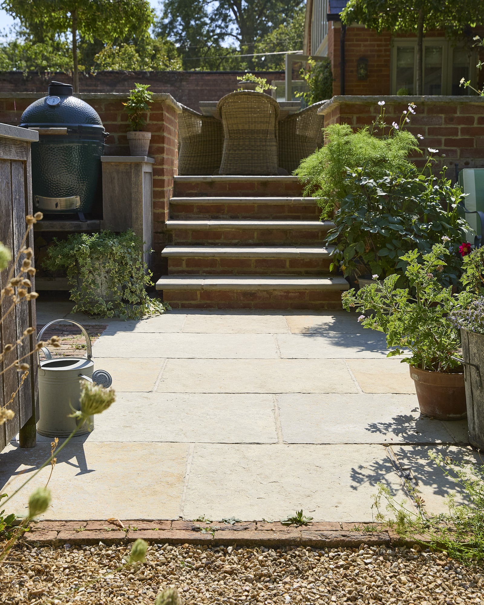 Trusloe Limestone Seasoned Finish paving and step treads in a walled courtyard with an outdoor kitchen and potted pelargoniums