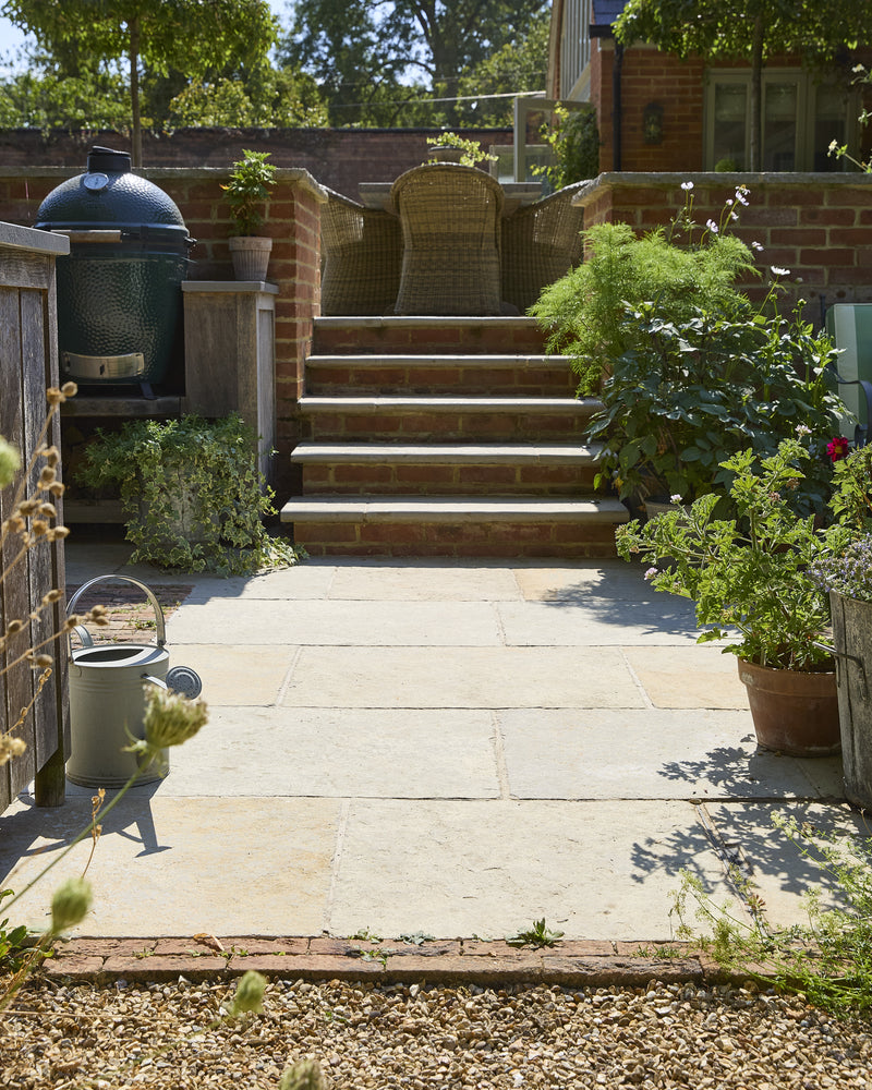Trusloe Limestone Seasoned Finish paving and step treads in a walled courtyard with an outdoor kitchen and potted pelargoniums
