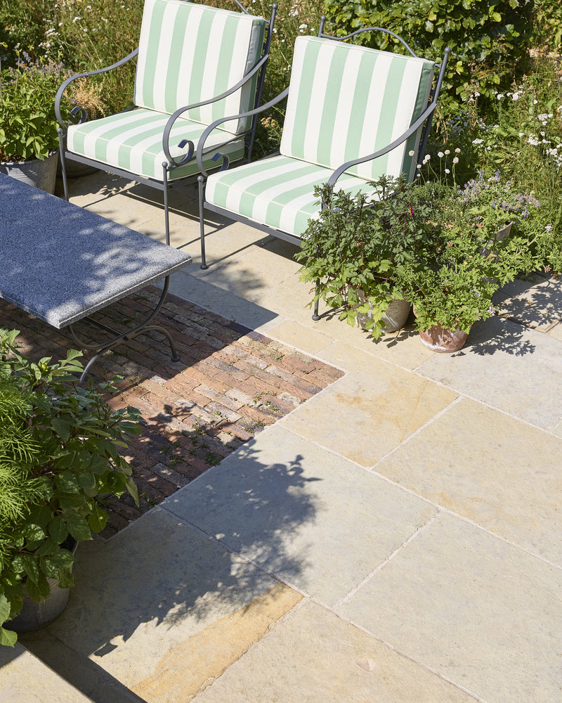 Trusloe Limestone Seasoned Finish paving laid around a reclaimed brick inset, with green striped garden chairs and terracotta pots