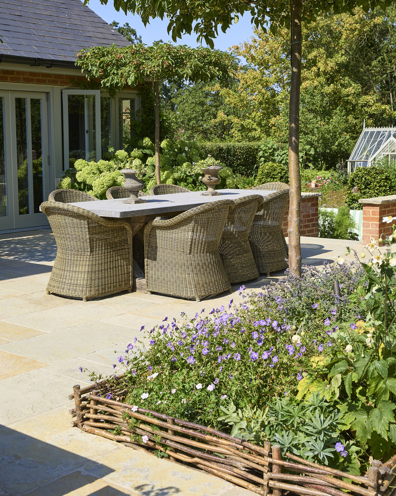 Trusloe Limestone Seasoned Finish paving beneath a stone-topped dining table and wicker chairs, shaded by pleached crab apple trees