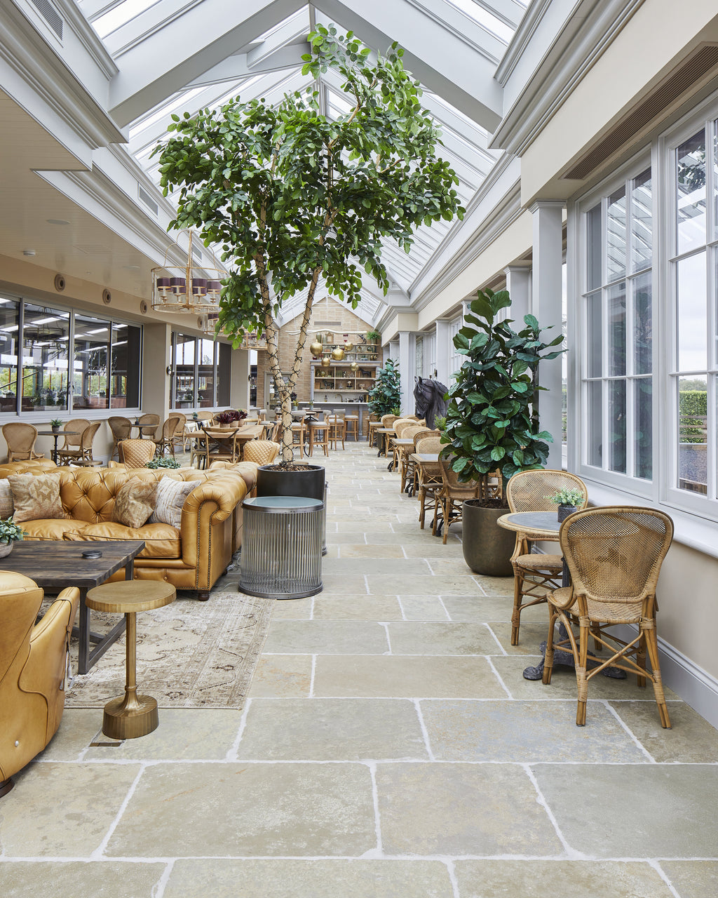 Trusloe Limestone Seasoned Finish flagstone flooring in a light-filled orangery with a central tree, tan leather sofas and rattan chairs