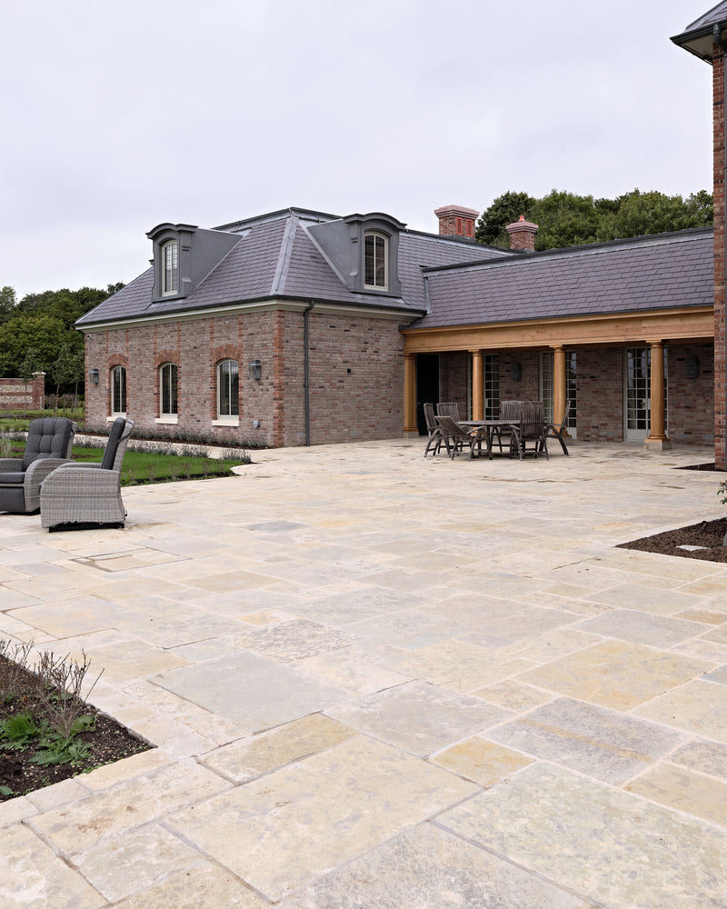 Trusloe Limestone Seasoned Finish paving across a large terrace outside a red brick house with an oak colonnade