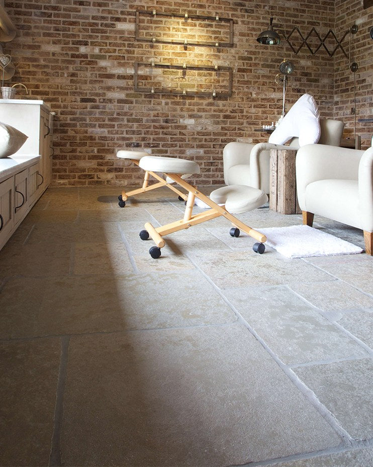 Trusloe Limestone Seasoned Finish flagstone floor in a relaxed brick-walled room with cream armchairs