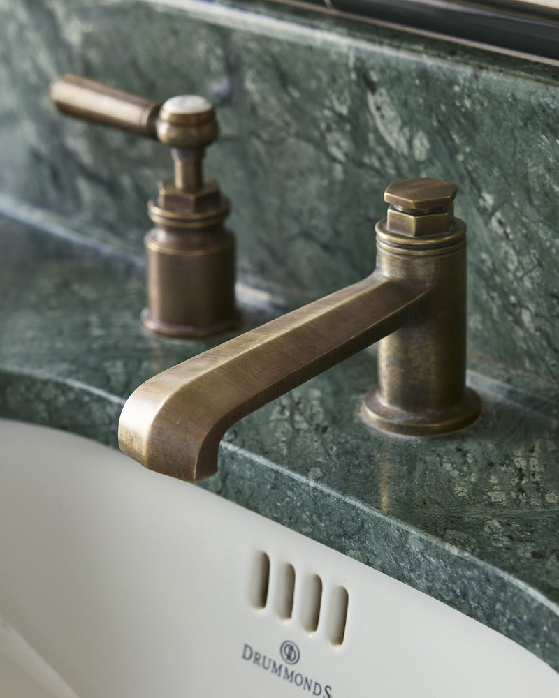 Close view of Verde Guatemala Marble Slab as a vanity top and upstand, showing the deep green ground and white veining, with an antique brass tap over a white ceramic basin