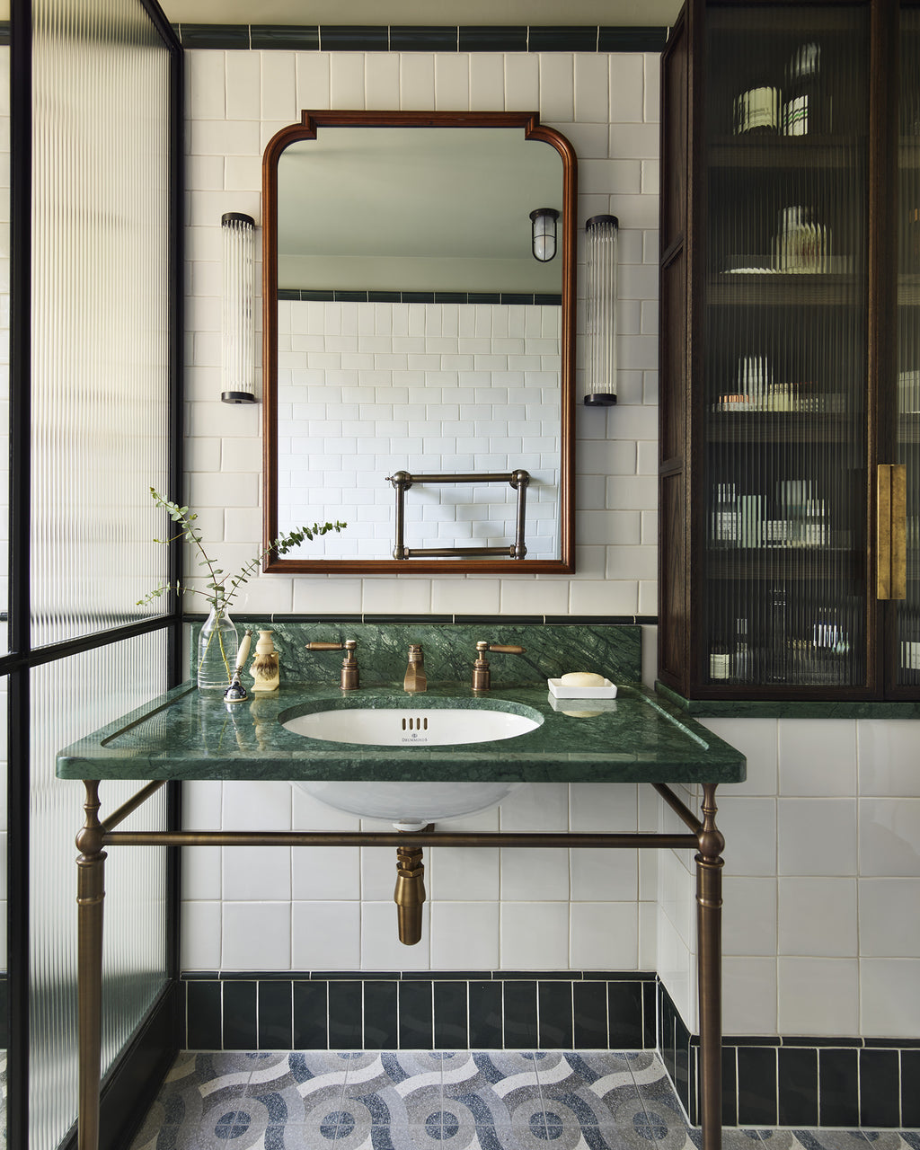 Verde Guatemala Marble Slab forming a washstand top on an antique brass frame, against white tiling with a dark green border and a patterned terrazzo floor