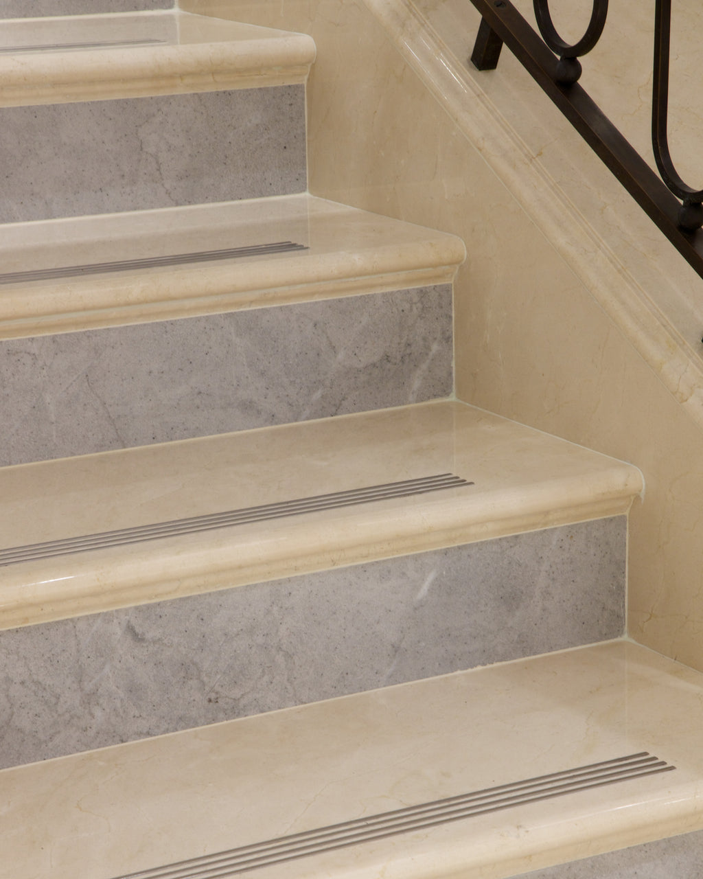 Versailles Creme Marble Slab used for staircase treads with contrasting grey risers, bullnose nosings and brass anti-slip inserts, beside a wrought iron balustrade