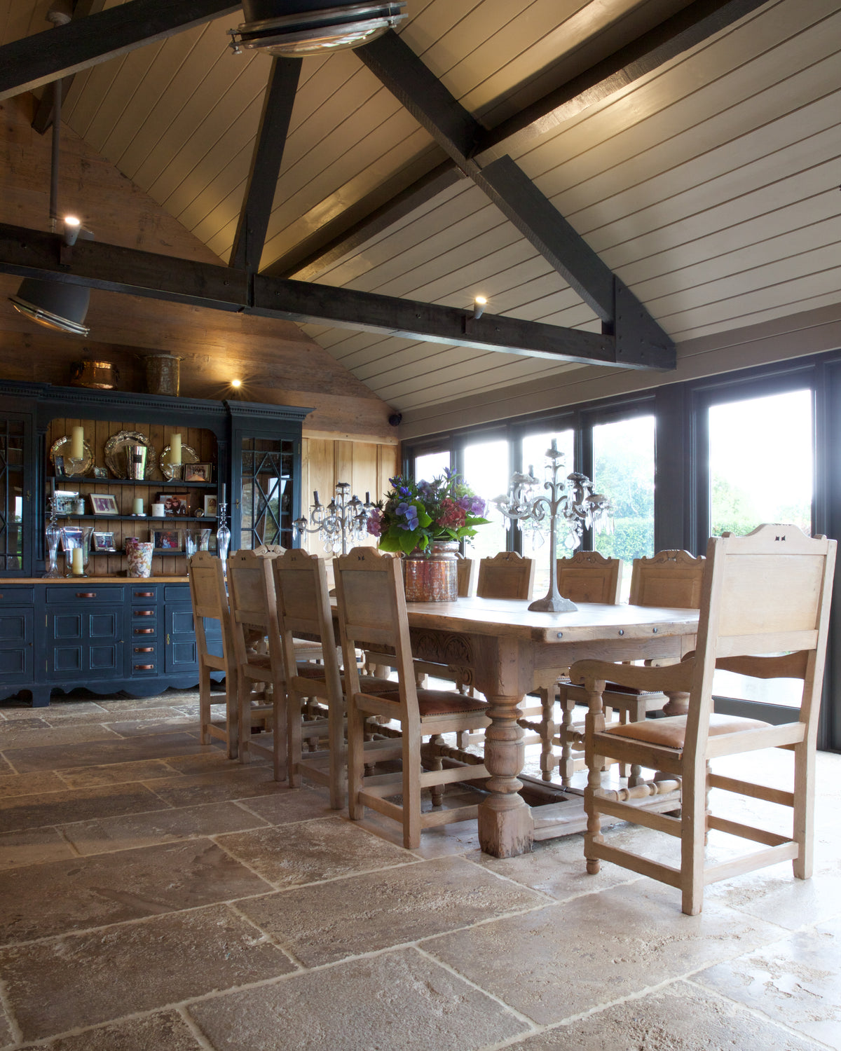 Vieux Bourgogne Limestone Ancient Finish across a barn dining room floor beneath an open trussed roof, with a long oak refectory table and a blue dresser