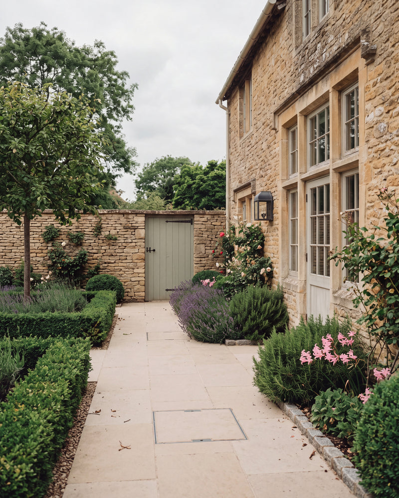 Wychwood Limestone Paving Tumbled & Etched Finish laid as a wide path through a walled Cotswold courtyard, with clipped box, lavender and roses against the honey stone farmhouse