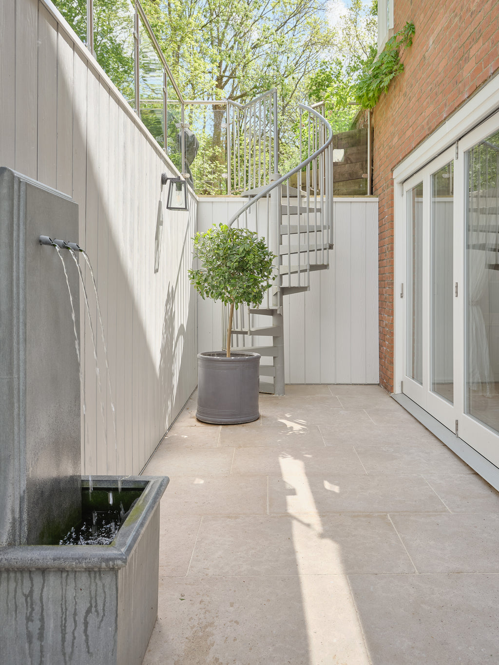 Wychwood Limestone Tumbled & Etched paving in a narrow courtyard with a water feature, bay tree and spiral staircase